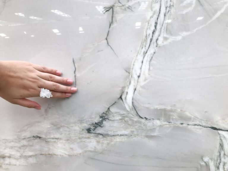 Hand touching a white Le Blanc quartzite slab with green veining by KJM Stones