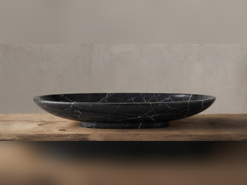 Black marble oval platter with white veining on a reclaimed wood shelf